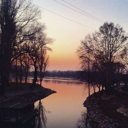 Silhouette bare trees by lake against sky during sunset