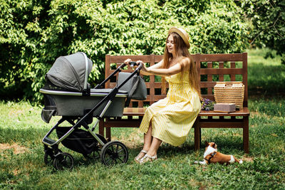 Mother walking with newborn baby in bassinet stroller in summer park in sunny day. strollers for