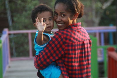 Portrait of smiling mother carrying son while standing outdoors