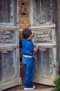 Disgruntled child is a traveler boy in a blue jumpsuit standing in the mountains in summer