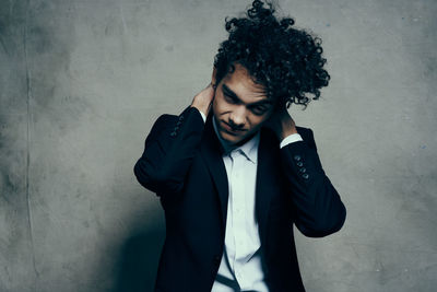 Young man looking away while standing against wall