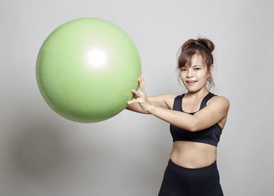 Woman exercising with green fitness ball against white background