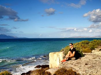 Woman sitting on rock looking at sea against sky