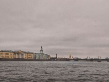 Buildings by sea against cloudy sky