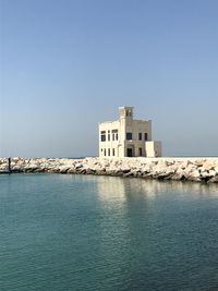 Buildings by sea against clear blue sky