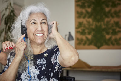 Smiling senior woman wearing headphones looking away while sitting with friend at home