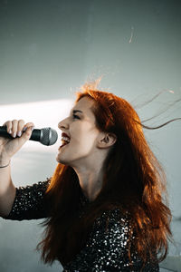 Portrait of redhead female singer woman in sparkly evening dress holding microphone on dark night
