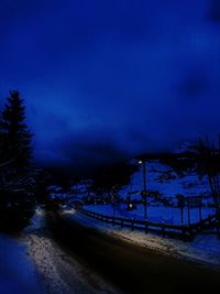 Road amidst trees against blue sky at night during winter