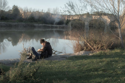 Side view of man sitting by lake against trees