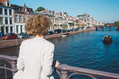 Rear view of woman standing by railing over canal in city