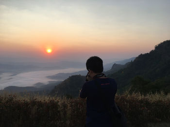 Rear view of man looking at mountain during sunset