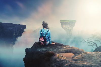 Rear view of woman sitting on rock formation against sky during sunset