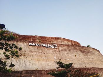 Low angle view of text on wall against clear sky