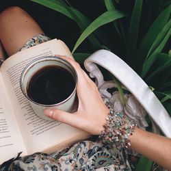 Midsection of woman with coffee cup and book by plants