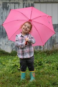 Full length portrait of smiling girl standing with umbrella on field