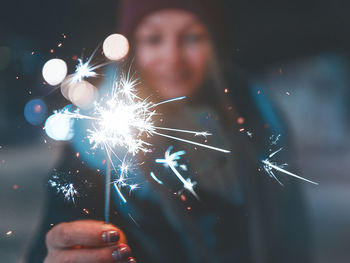 Close-up of woman holding sparkler burning at night