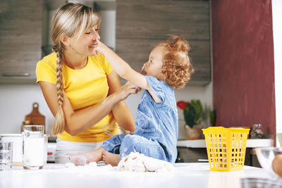 Mom and daughter are cooking in the kitchen, smiling and playing. on the table is the dough