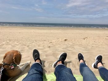 Low section of people standing on beach against sky