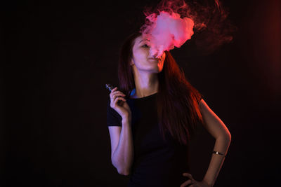 Young woman smoking against black background