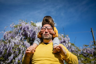 Low angle view of man standing against sky while his child closes his eyes