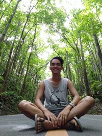 Portrait of smiling young woman sitting on land in forest