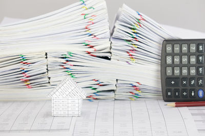 Close-up of model house with pencil and calculator by stacked files against gray background