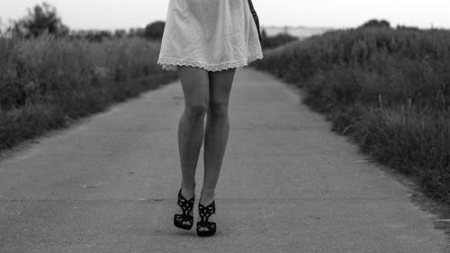 Low section of woman walking on road amidst grass