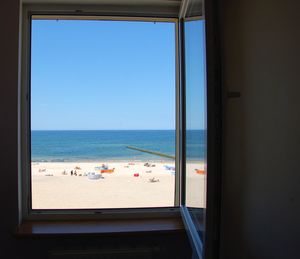 Scenic view of sea against clear blue sky seen through window