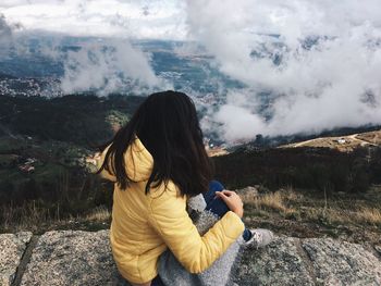 Rear view of woman sitting on mountain against sky