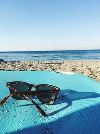 Sunglasses on beach against clear sky