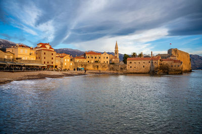 Buildings by river against sky