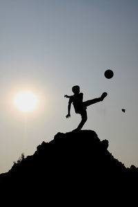 Low angle view of silhouette boy playing with ball against sky during sunset