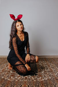 Portrait of young woman sitting against wall