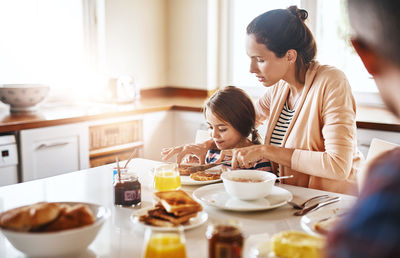 Woman with daughter preparing breakfast at dining table