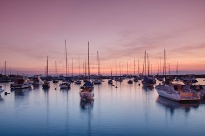 Sailboats moored in harbor at sunset