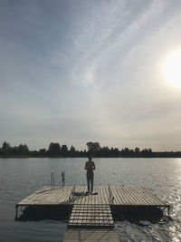 Rear view of man walking on pier against sky during sunrise 