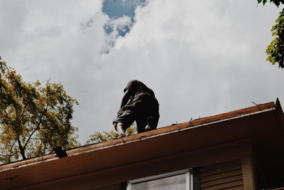 Low angle view of man standing on house roof against sky
