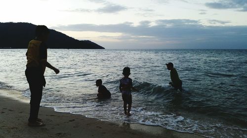 Children playing on beach against sky during sunset