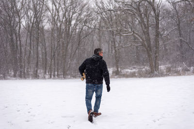 Rear view of man walking on snow covered land against trees