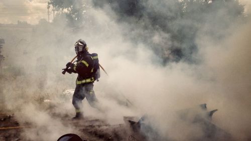 Full length of firefighter walking amidst smoke