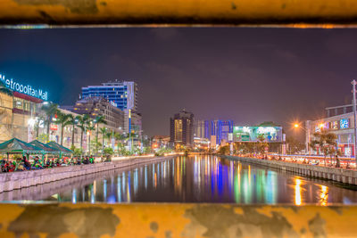 Illuminated bridge over river by buildings against sky at night