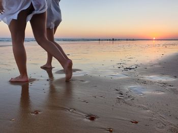 Low section of woman on beach against sky during sunset