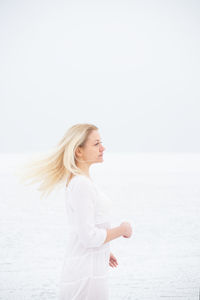 Side view of woman standing in sea against sky