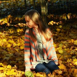 Girl sitting on maple leaves at park during autumn