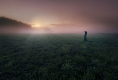 Silhouette person standing on field against sky during sunset