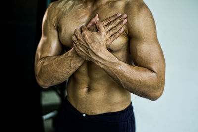 Midsection of shirtless man with hand on chest