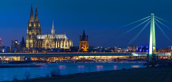 Illuminated bridge over river and buildings in city at night