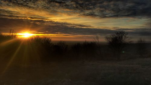 Scenic view of landscape against dramatic sky during sunset