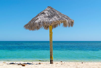 Thatched parasol on beach against clear blue sky