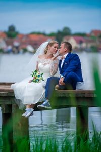 Romantic bride and groom sitting on wooden pier over lake